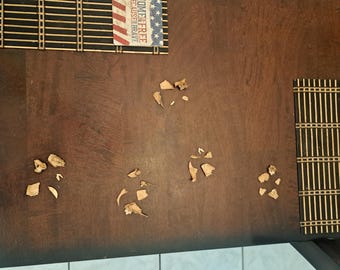 May include: A close-up of a wooden table surface with several small pieces of brown, dried fruit scattered across it. The table is a dark brown color and has a smooth, polished finish.