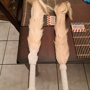 May include: Two handmade, light-colored horsehair fly whisks. The handles are wrapped in white beads. The whisks are displayed on a dark brown surface with bamboo placemats and small patriotic signs.