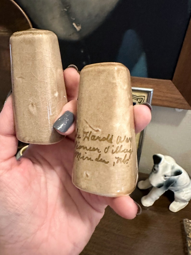 May include: Two small, brown ceramic salt and pepper shakers with gold lettering. The shaker on the right says "The Hard Way", "Sometimes I'll lay", "Mine down in it!"