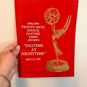 May include: A bright red program booklet for the 1998-1999 Twenty Sixth Annual Daytime Emmy Awards titled "Daytime at Nighttime" dated May 21, 1999, featuring a gold-colored graphic of the Emmy statuette on the right side of the cover.