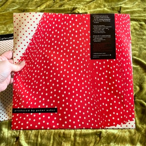 May include: Red vinyl record with white polka dots. The back cover features text that reads "produced by peter asher" and credits for the recording and production of the album.