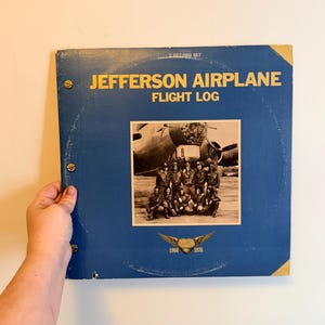 May include: A vintage blue vinyl record album titled "Jefferson Airplane Flight Log." The album cover features a black and white photo of the band and a plane. The album is a 2-record set.