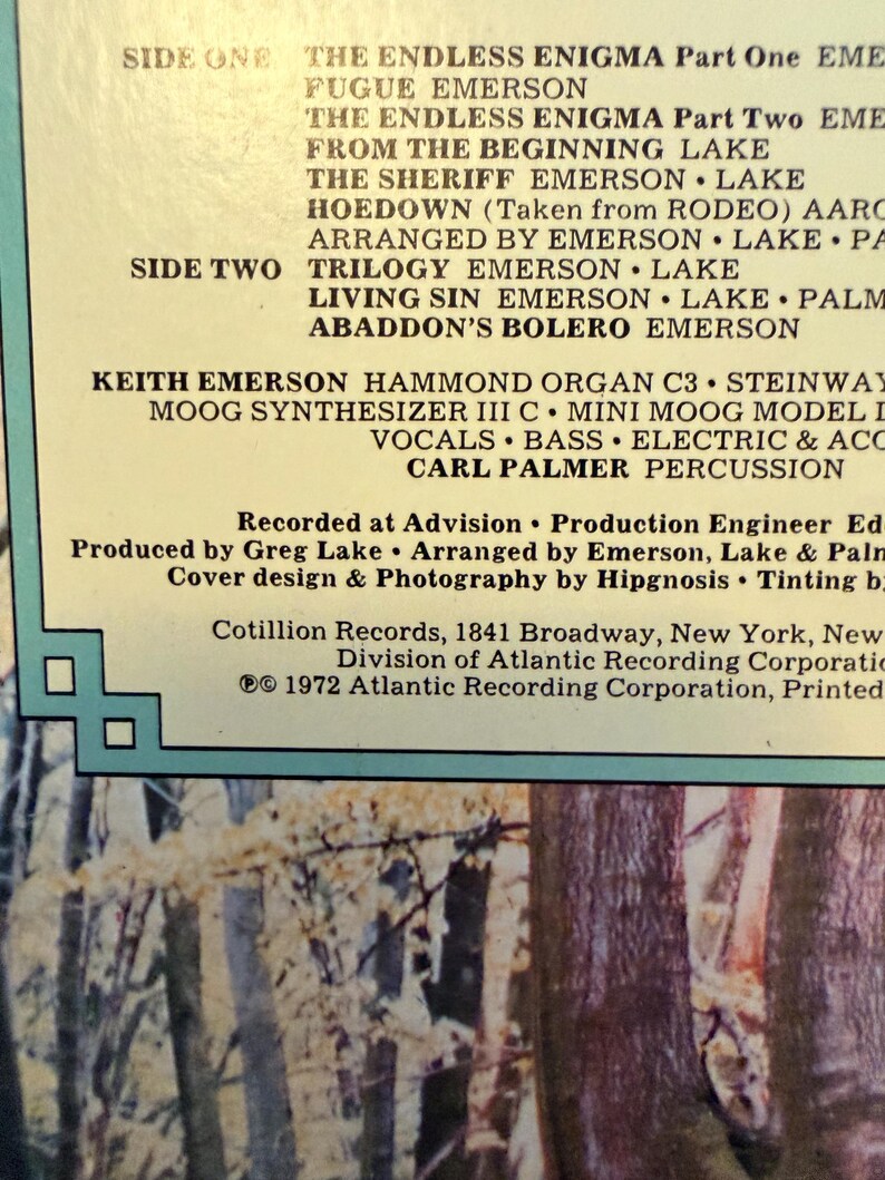 May include: Close-up of a vintage vinyl record album cover. The album's tracklist is displayed in bold, black text against a cream-colored background. The album title and artist are not visible. The cover features a nature scene with trees and foliage.