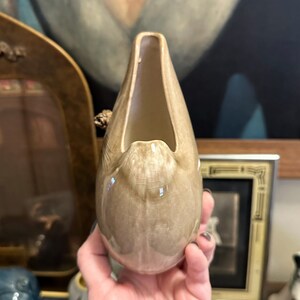 May include: A light brown ceramic vase shaped like a bird's head with a wide open beak. The vase has a speckled glaze and a glossy finish.
