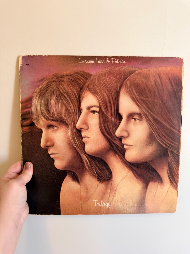 May include: Vintage vinyl record album cover for Emerson, Lake & Palmer's "Trilogy." The cover art features three side profiles of individuals with long hair. The album title and band name are printed on the cover.