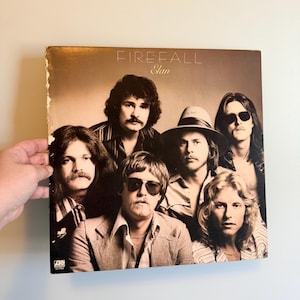 May include: A vintage vinyl record album cover featuring the band Firefall. The album cover is a sepia tone with the band members in the center. The album title "Elan" is printed at the top.