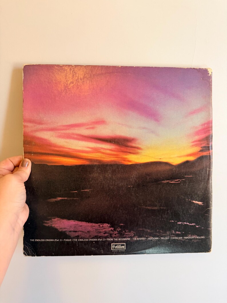 May include: Vintage vinyl record album cover featuring a sunset landscape with vibrant pink, orange, and purple hues. The album cover has the text "THE ENDLESS ENIGMA" and other song titles. The Cotillion label is visible.