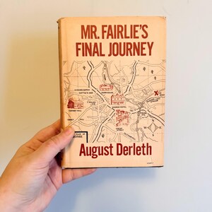 May include: A vintage book titled "Mr. Fairlie's Final Journey" by August Derleth. The cover is a light orange color with a map illustration and red text. The book is held by a hand.