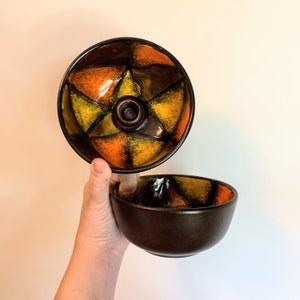 May include: A set of two ceramic bowls with a geometric pattern in shades of orange, yellow, and brown. The bowls are designed with a star shape in the center.
