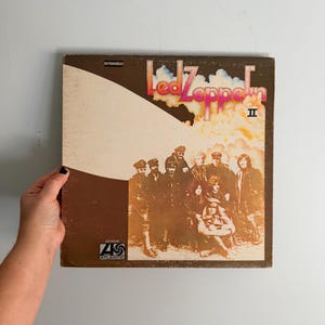 May include: Vintage Led Zeppelin II vinyl record album cover. The album cover is brown and features a group of people in sepia tones. The band's name is in red and pink lettering. The Atlantic Records logo is visible.