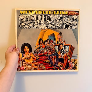 May include: Vintage vinyl record album cover for West, Bruce & Laing, titled "Whatever Turns You On." The cover art features a cartoon-style illustration of the band members and a diner scene with burgers and a red carpet.