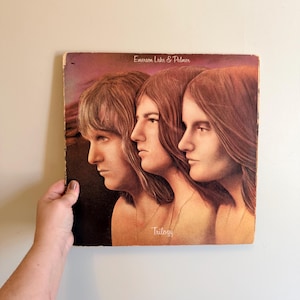 May include: Vintage vinyl record album cover for Emerson, Lake & Palmer's "Trilogy." The cover art features three side profiles of people with long hair, in shades of brown and gold. The album title and band name are printed on the cover.