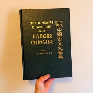 May include: A dark green hardcover book titled "DICTIONNAIRE CLASSIQUE de la LANGUE CHINOISE" in gold lettering. The book also has Chinese characters in gold. The author's name, F. S. COUVREUR S. J., is printed at the bottom.
