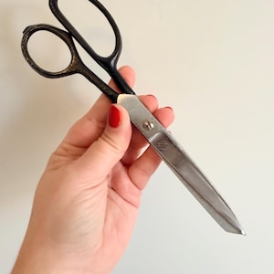 May include: A pair of vintage scissors with black handles and silver blades. The scissors have a classic design, with large finger holes and a pointed tip. The blades are sharp and ready for cutting.