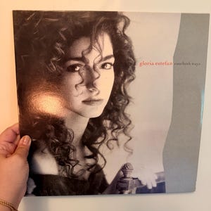 May include: A square vinyl record album cover featuring a black and white portrait of Gloria Estefan with curly hair. The text "gloria estefan" appears in red and "cuts both ways" in black on the right side against a light gray background.