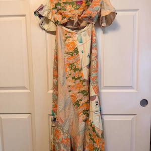 May include: A floor-length dress featuring a patchwork design with various floral and geometric patterns in shades of orange, green, blue, and cream. The dress has short flutter sleeves, a tie-front bodice, and a cutout at the midriff area.