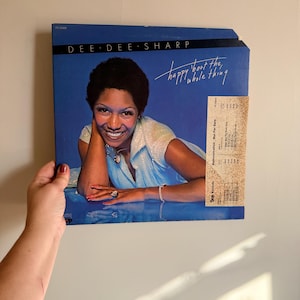 May include: A vintage vinyl record album cover featuring Dee Dee Sharp, with the album title "happy bout the whole thing" in white script on a blue background. A promotional sticker is attached to the album cover.