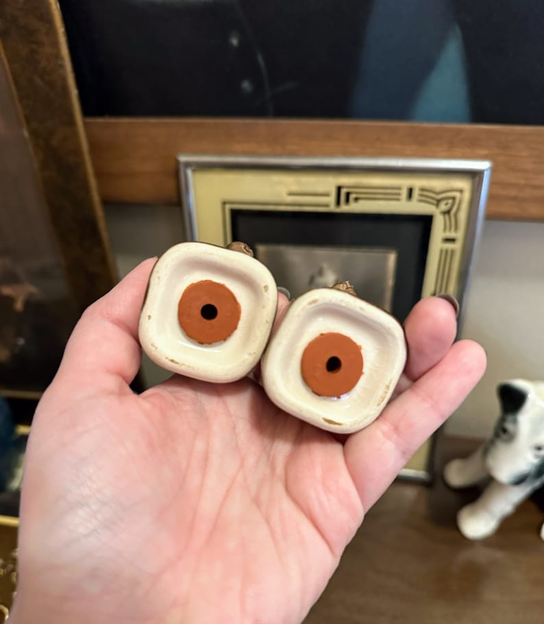 May include: Two ceramic salt and pepper shakers with brown rubber stoppers on the bottom. The shakers are white with gold accents.