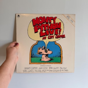 May include: A vintage Monty Python Live! album cover. The cover features a cartoon illustration with the text "MONTY PYTHON LIVE! AT CITY CENTER" in red and yellow. The album cover also lists the performers' names.