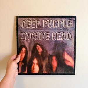 May include: A vintage vinyl record album cover for Deep Purple's "Machine Head." The album cover features the band members with the album title in a raised, textured font. The background is a dark, blurred image.