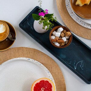 May include: A breakfast setting featuring a coffee cup, a plate with a croissant, and a halved grapefruit. A small vase with flowers sits on a dark blue tray, with a bowl of sugar cubes.