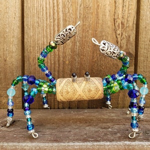 May include: A beaded crab sculpture made with green, blue, and silver beads. The crab is made on a wire frame and has a cork body.