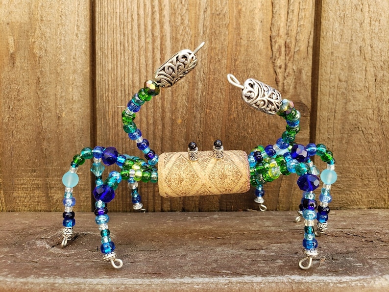 May include: A beaded crab sculpture made with green, blue, and silver beads. The crab is made on a wire frame and has a cork body.