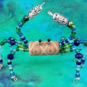 May include: A beaded crab sculpture with a cork body, blue and green glass beads, and silver wire legs. The crab is posed with its claws raised.