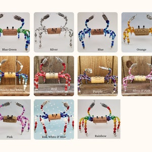 May include: A collection of 12 beaded crab ornaments, each with a different color scheme. The crabs are made with glass beads and have a cork body. The colors include blue green, silver, blue, orange, beachy blue white, red, silver and pink, purple, pink, red, white and blue, and rainbow.