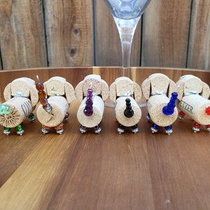 May include: Seven miniature dachshund figurines made from wine corks with beaded tails in various colors, including green, brown, purple, black, blue, and red. The corks are labeled "Fetzer".