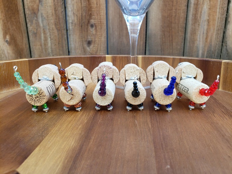 May include: Seven miniature dachshund figurines made from wine corks with beaded tails in various colors, including green, brown, purple, black, blue, and red. The corks are labeled "Fetzer".