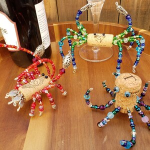 May include: Three colorful beaded bottle stoppers shaped like a crab, octopus, and spider. Each stopper is made with glass beads and has a cork base.