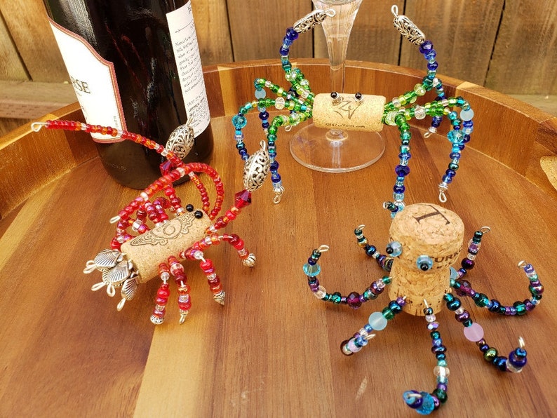 May include: Three colorful beaded bottle stoppers shaped like a crab, octopus, and spider. Each stopper is made with glass beads and has a cork base.