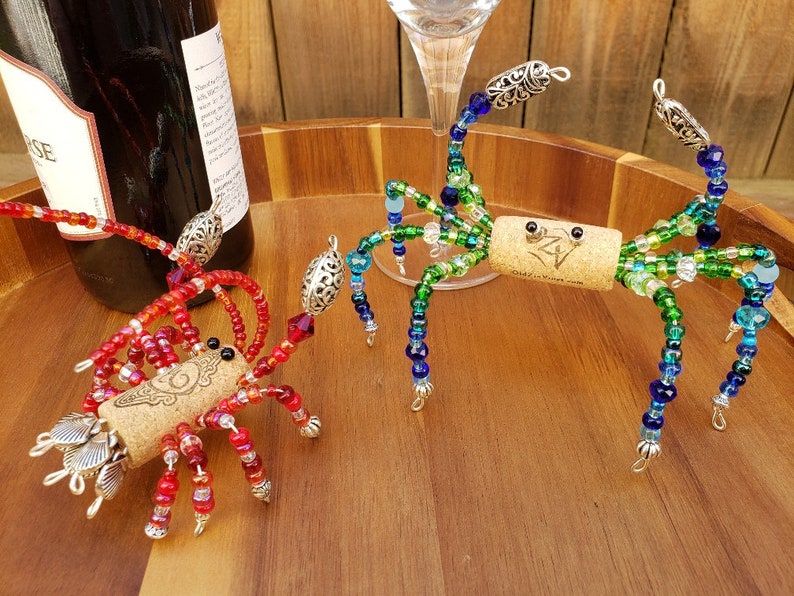 May include: Two beaded wine bottle stoppers shaped like crabs. One is red and the other is green and blue. Both have cork bodies and silver accents.