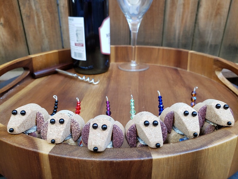 May include: Eight wine bottle stoppers shaped like brown and white dachshunds with black eyes. Each stopper has a different colored beaded tail.