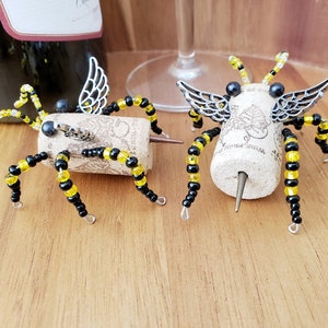 Puede incluir: Dos tapones para botellas de vino con forma de ara&ntilde;a con cuentas negras y amarillas y alas plateadas. Las ara&ntilde;as est&aacute;n hechas de corcho y tienen una punta de metal para insertar en la botella.