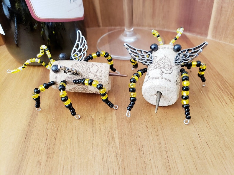 Puede incluir: Dos tapones para botellas de vino con forma de ara&ntilde;a con cuentas negras y amarillas y alas plateadas. Las ara&ntilde;as est&aacute;n hechas de corcho y tienen una punta de metal para insertar en la botella.