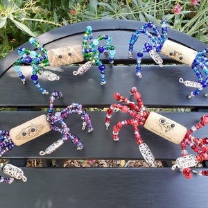 May include: Five colorful beaded spider ornaments made with wine corks. Each spider has a different color scheme, including blue, green, purple, red, and a combination of blue and green.