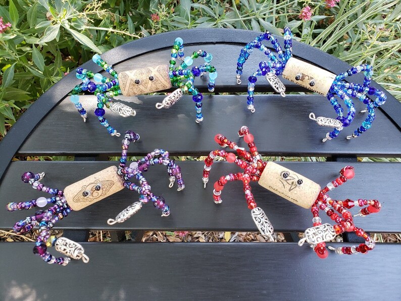 May include: Five colorful beaded spider ornaments made with wine corks. Each spider has a different color scheme, including blue, green, purple, red, and a combination of blue and green.
