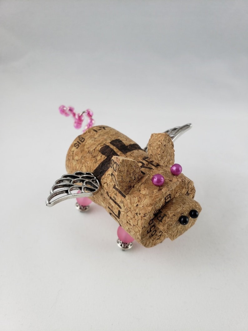 May include: A small, winged pig figurine made from a wine cork. The pig has pink beads for eyes and a pink beaded tail. The wings are made of silver metal.
