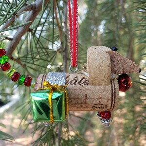 May include: A cork dachshund Christmas ornament with a red ribbon, green gift box, and red and green beads. The cork is labeled "Chateau Diam 5".