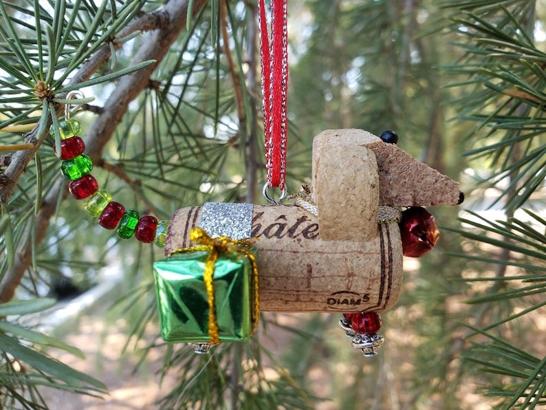 May include: A cork dachshund Christmas ornament with a red ribbon, green gift box, and red and green beads. The cork is labeled "Chateau Diam 5".