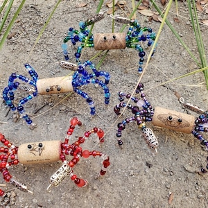 May include: Five colorful beaded crab ornaments made from wine corks. Each crab has a different color scheme, including blue, green, purple, and red. The crabs have silver accents and are a fun and whimsical decoration.