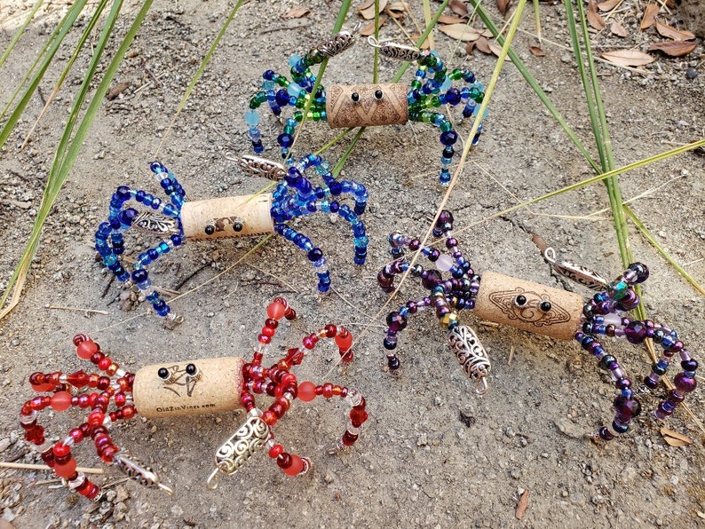 May include: Five colorful beaded crab ornaments made from wine corks. Each crab has a different color scheme, including blue, green, purple, and red. The crabs have silver accents and are a fun and whimsical decoration.