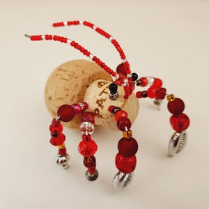 May include: A red and silver beaded spider with a cork body. The cork has the word "Etta" written on it.