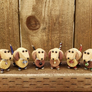 May include: Six miniature dachshund figurines made from wine corks and decorated with beads. The dachshunds are brown and have black eyes. Each dachshund has a different colored beaded tail.