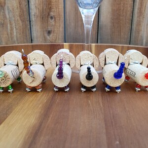 May include: Seven miniature dachshund bottle stoppers made from wine corks with beaded tails in various colors, including green, brown, purple, black, blue, and red.