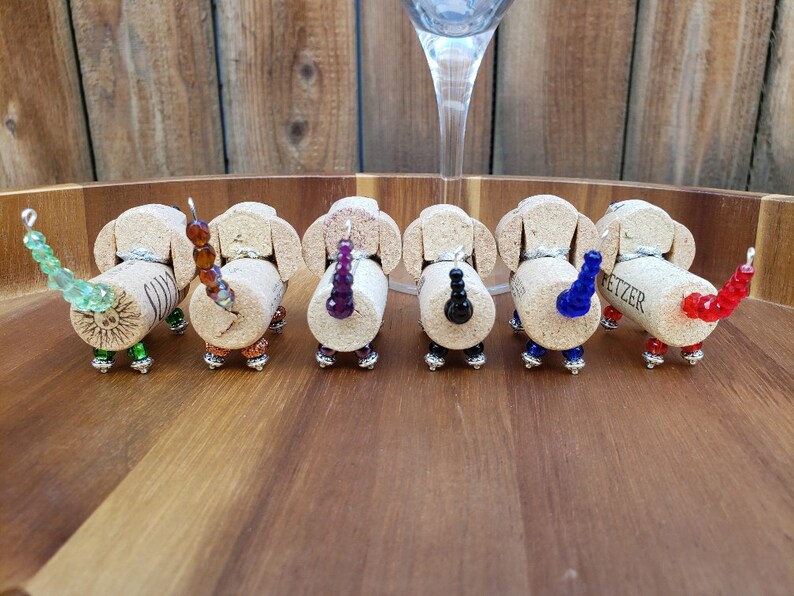 May include: Seven miniature dachshund bottle stoppers made from wine corks with beaded tails in various colors, including green, brown, purple, black, blue, and red.