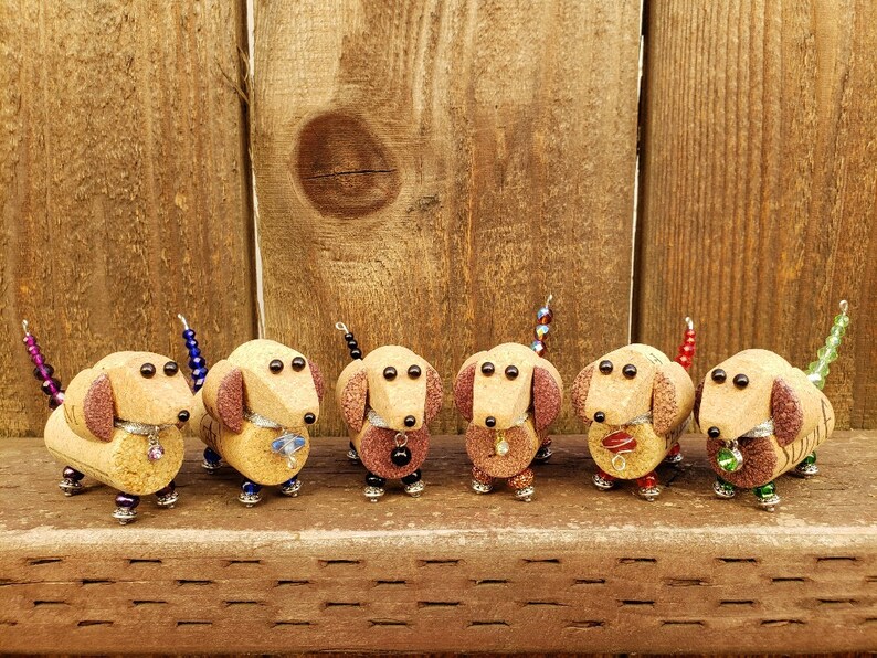 May include: Six miniature dachshund figurines made from wine corks, each with a different colored beaded tail and decorative accents.