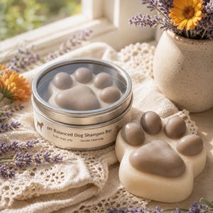 May include: A dog shampoo bar in the shape of a paw print, displayed next to a tin with the same design. The tin reads "pH Balanced Dog Shampoo Bar" and "Gentle Cleansing". The scene includes lavender and a vase with a yellow flower.